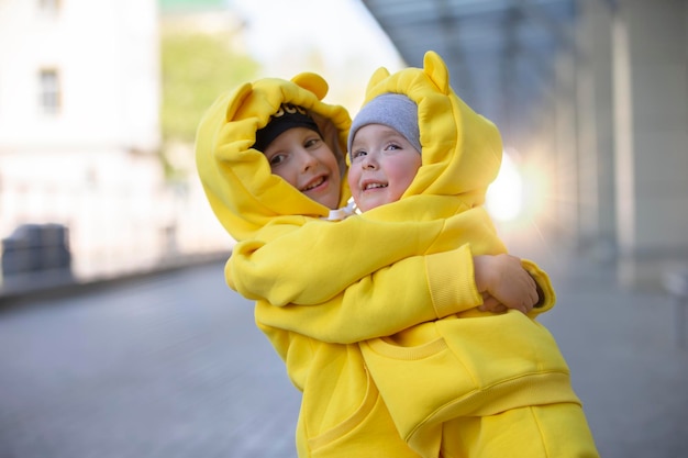 Kleiner Bruder und Schwester Lustige Kinder Junge und Mädchen in gelben Anzügen umarmen sich