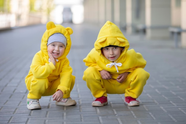 Kleiner Bruder und Schwester Lustige Kinder Junge und Mädchen in gelben identischen Anzügen spielen im Freien