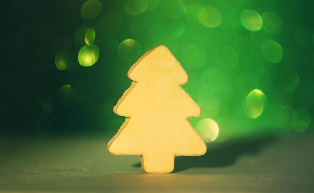 Kleiner dekorativer hölzerner Weihnachtsbaum auf funkelndem Glitzerhintergrund