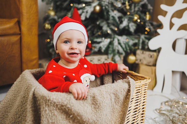 kleiner einjähriger Junge in der Nähe des Weihnachtsbaums eine Idee für ein Kinderfoto für das neue Jahr Studio Neujahrsdekoration Weihnachtsgeschenke rotes Kinderfestkostüm