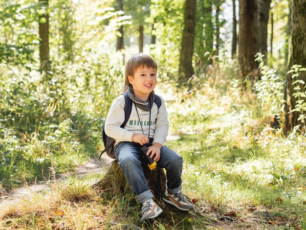 Foto kleiner entdecker auf wanderung im wald junge mit fernglas sitzt auf stumpf sommerreise für touristen