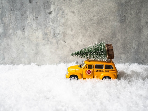 Kleiner gelber Spielzeugschulbus trägt einen Weihnachtsbaum auf dem Dach