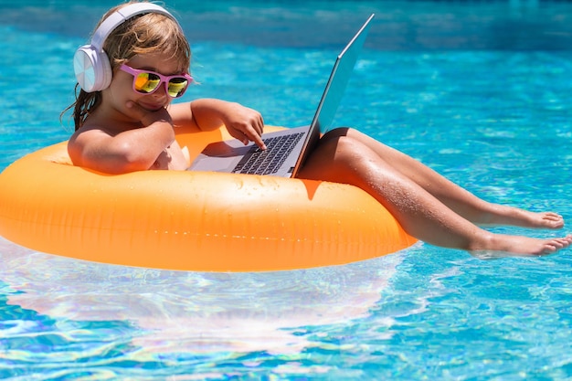 Kleiner Geschäftsmann, der an einem tropischen Strandkind mit Laptop im Schwimmbad am Sommertag arbeitet