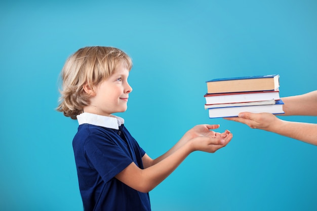 Kleiner glücklicher blonder Schuljunge, der Bücher in der Bibliothek nimmt