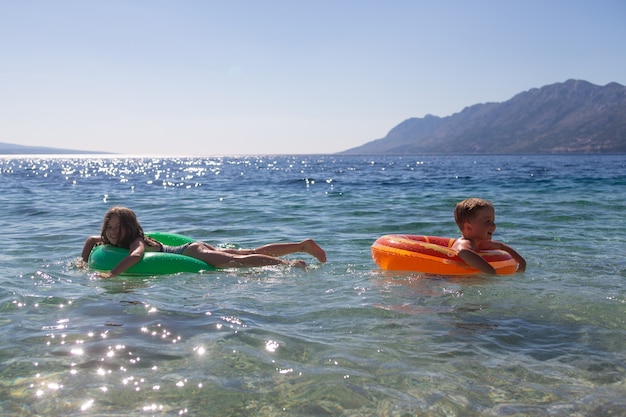 kleiner glücklicher Junge und Mädchen, die im Meer auf einem aufblasbaren Ring schwimmen, Konzept der Kinder- und Familiensommerferien