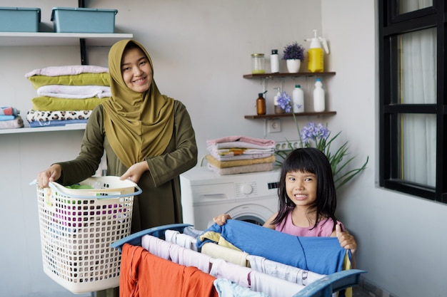 Kleiner Helfer der muslimischen asiatischen Mutter und des Kindermädchens im Waschraum nahe der Waschmaschine