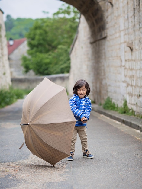 Foto kleiner hübscher junge, der mit regenschirm im freien spielt