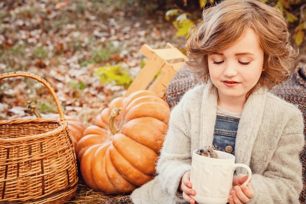 Kleiner Igel in den Händen eines süßen Mädchens Porträt von Kind mit Haustier Beige Hintergrund Herbst Hintergrund Kürbisse Heuhaufen und rote Blätter Erntezeit