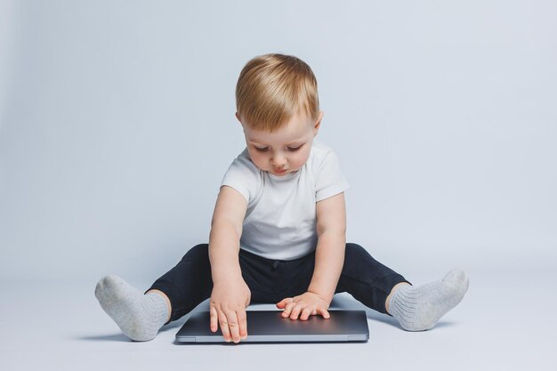 Kleiner intelligenter Junge, 34 Jahre alt, sitzt mit einem Laptop auf weißem Hintergrund Ein Kind in einem weißen T-Shirt und einer schwarzen Hose sitzt an einem Laptop und sieht auf den Bildschirm Moderne progressive Kinder