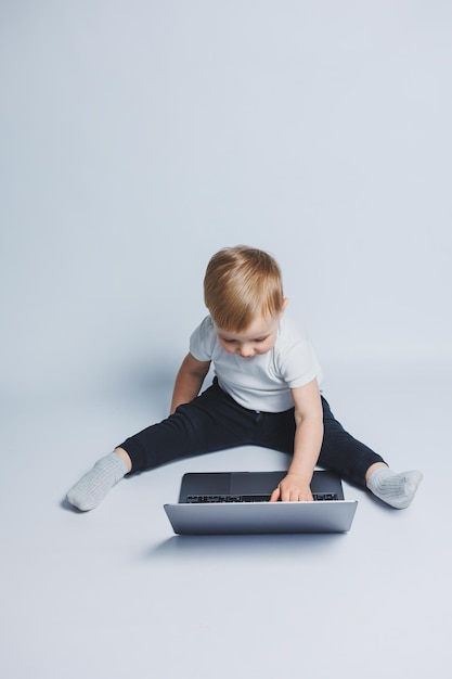 Kleiner intelligenter Junge, 34 Jahre alt, sitzt mit einem Laptop auf weißem Hintergrund Ein Kind in einem weißen T-Shirt und einer schwarzen Hose sitzt an einem Laptop und sieht auf den Bildschirm Moderne progressive Kinder