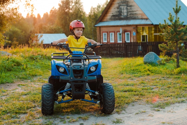 Kleiner Junge 5 Jahre Kinder ATV fährt im Dorfhaus in den Sommerferien untergehende Sonne. Quad-Bike