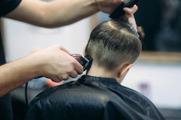 Kleiner Junge auf einem Haarschnitt im Friseur sitzt auf einem Stuhl