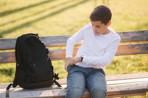 Kleiner Junge aus seiner Tasche Smartphone nehmen Teenager sitzen auf der Bank im Park