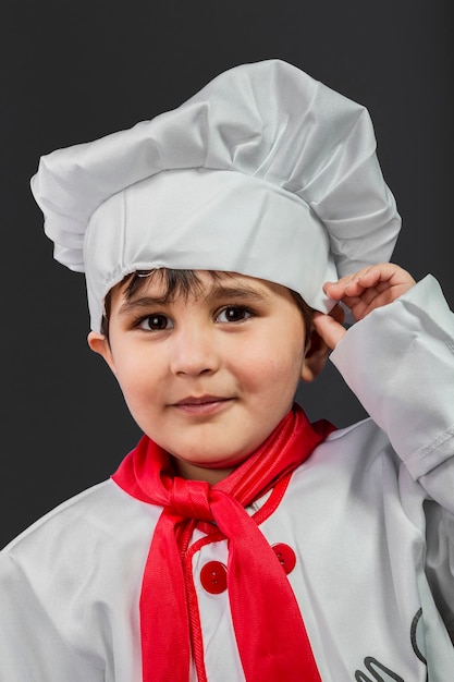 Kleiner Junge bereitet gesundes Essen in der Küche auf grauem Hintergrund zu, Kochmütze