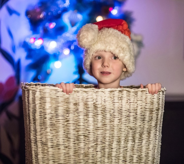 Kleiner Junge, der als Weihnachtsmann verkleidet ist und in einem großen Korb sitzt