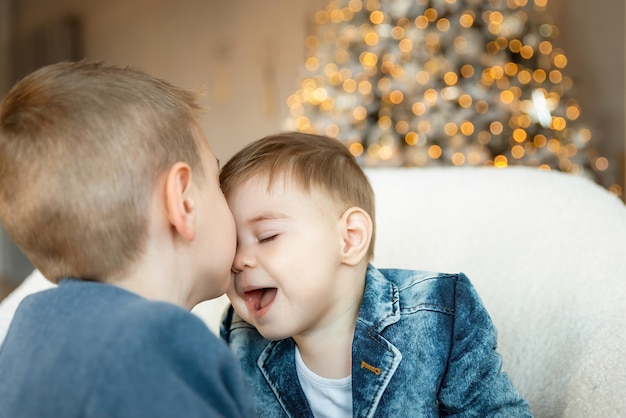 Kleiner Junge, der am Weihnachtsmorgen seinen kleinen Bruder küsst. Kinderjunge, der zärtlich die Stirn seines jüngeren Bruders küsst. Das Konzept der Liebe und Freundschaft zwischen Geschwistern. Silvester.