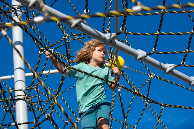 Kleiner Junge, der an der Affenstange an seiner Hand hängt, um im Seilpark auf dem Spielplatz im Freien zu trainieren