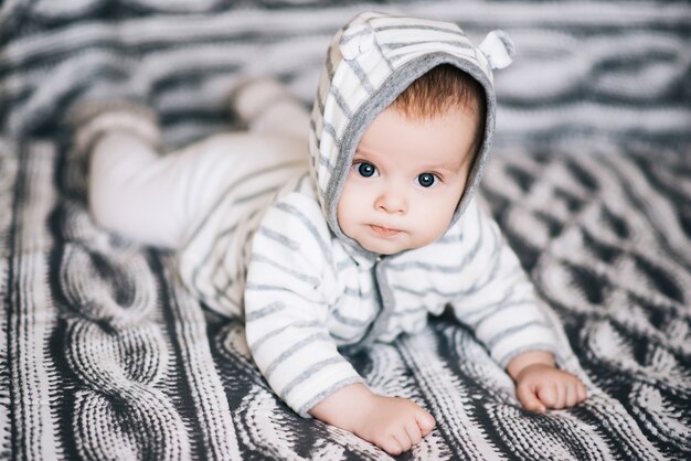 Kleiner Junge, der auf Bauch liegt und eine Weile seinen Kopf hebt und überrascht aussieht und süß, neugeboren lächelt