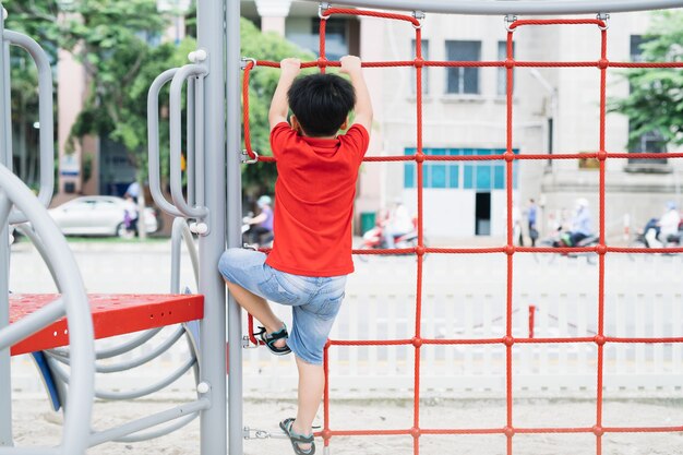 Kleiner Junge, der auf dem Klettergerüst am Spielplatz spielt