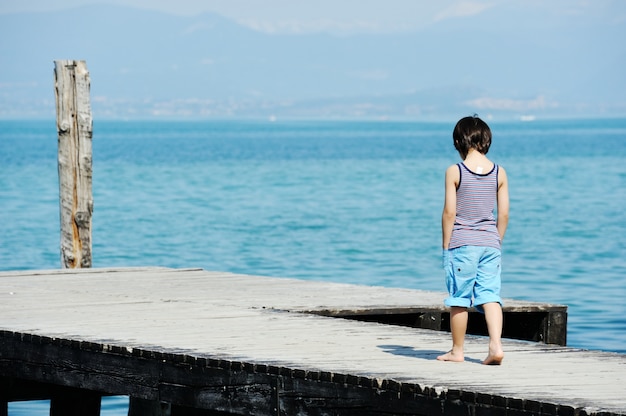 Kleiner Junge, der auf Dock durch schönes Meer geht