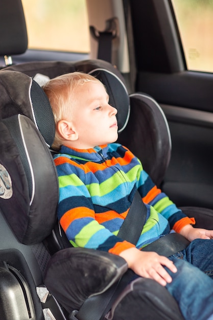 Kleiner Junge, der auf einem Autositz sitzt, schnallte sich im Auto an.