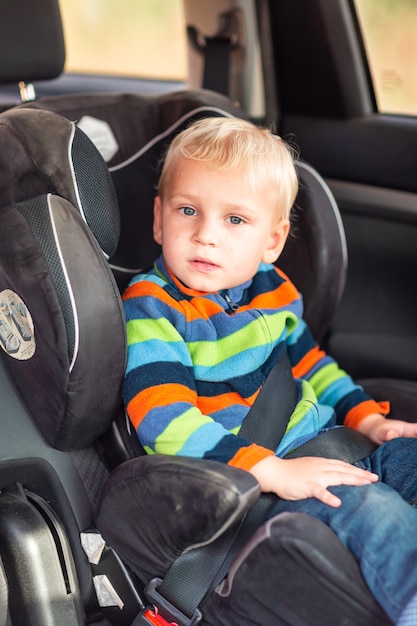 Kleiner Junge, der auf einem Autositz sitzt, schnallte sich im Auto an.