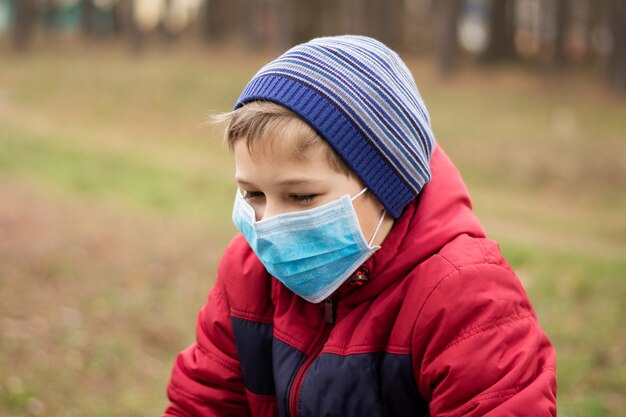 Kleiner Junge, der auf öffentlichem Spielplatz in der medizinischen Maske spielt, um sich vor Covid-19 zu schützen