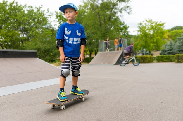 kleiner Junge, der auf seinem Skateboard in einem Skatepark steht und etwas in der Ferne mit ernstem Gesichtsausdruck beobachtet