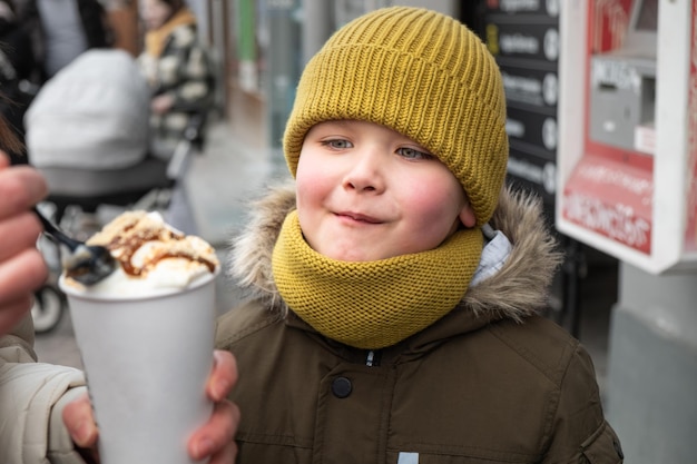 Kleiner Junge, der draußen mit Karamelllatte mit Löffel füttert