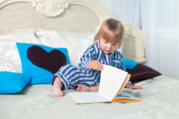 Kleiner Junge, der ein Buch auf dem Bett liest