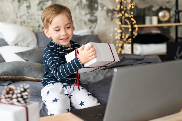 Foto kleiner junge, der ein geschenk hält, während video jemanden anruft