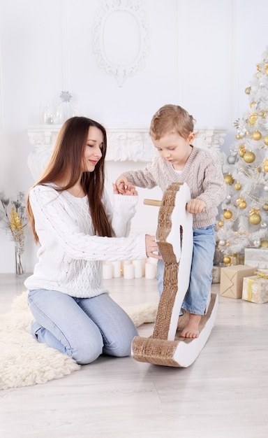 Kleiner Junge, der ein Papppferd nahe dem Weihnachtsbaum reitet