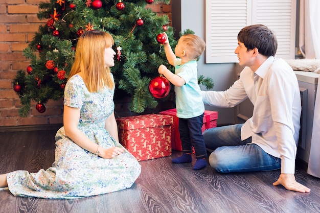 Kleiner Junge, der ein Weihnachtsbaumspielzeug verziert. Feiertags-, Geschenk- und Neujahrskonzept.