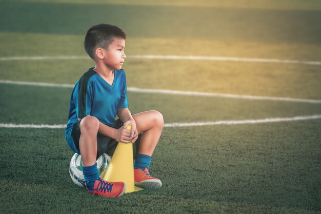 Kleiner Junge, der eine Pause auf Fußballtrainingsfeld macht