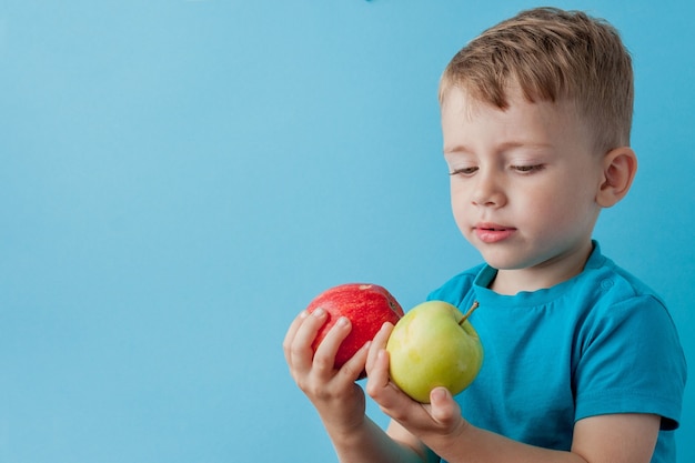 Kleiner Junge, der einen Apfel in seinen Händen auf blauem Hintergrund hält