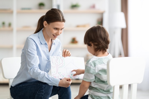 Kleiner Junge, der einer professionellen Psychologin, die die psychische Gesundheit von untersucht, ein Bild beschreibt