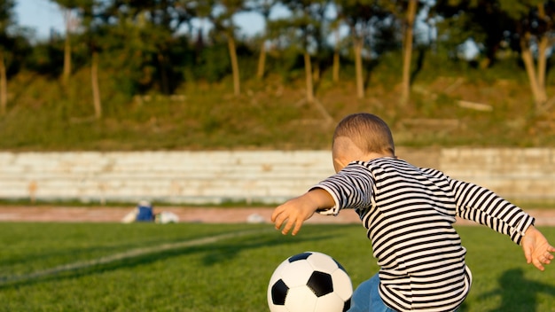 Kleiner Junge, der Fußball spielt oder Fußball, der einen Ball tritt
