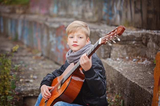 Kleiner Junge, der Gitarre am Herbstkältetag spielt.