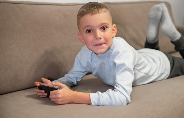 Kleiner Junge, der Handyspiel auf dem Smartphone spielt, sitzt auf einem Sofa, Draufsicht Kinderfreizeit zu Hause Video