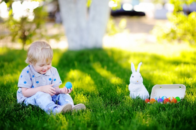 Kleiner Junge, der im Frühjahr für Garten Ostereies am Ostertag jagt. Nettes kleines Kind mit traditionellem Häschen Fest feiernd