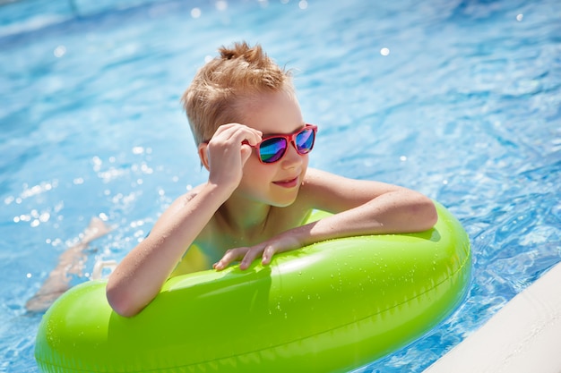 Kleiner Junge, der im Pool mit großem hellgrünem Gummiring schwimmt