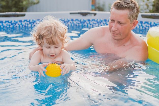 Kleiner Junge, der im Pool spielt und mit seinem Vater schwimmen lernt