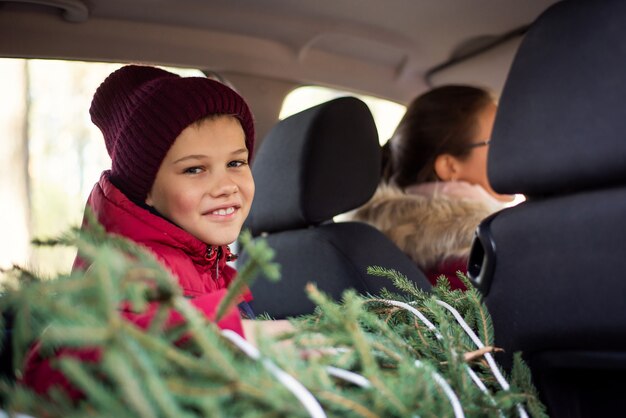 Kleiner Junge, der in einem Auto mit Weihnachtsbaum sitzt