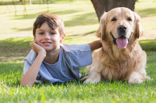 Kleiner Junge, der Kamera mit seinem Hund im Park betrachtet