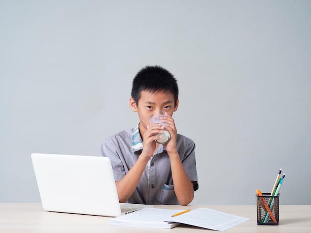 Kleiner Junge, der Milch trinkt, während er online zu Hause studiert