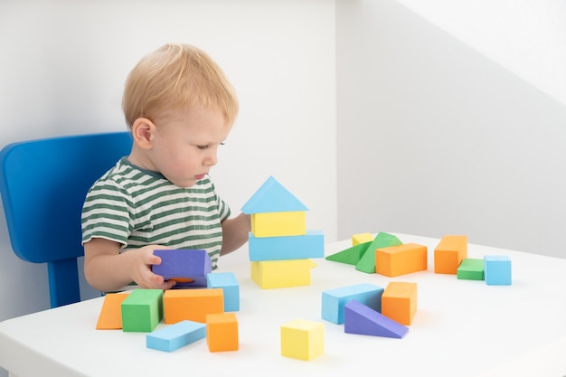 Kleiner Junge, der mit bunten Blöcken am Tisch auf weißem Hintergrund spielt.