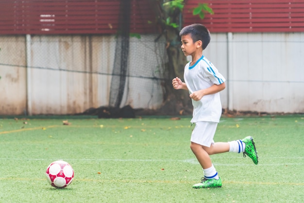 Kleiner Junge, der mit Fußball im Fußballfeld läuft