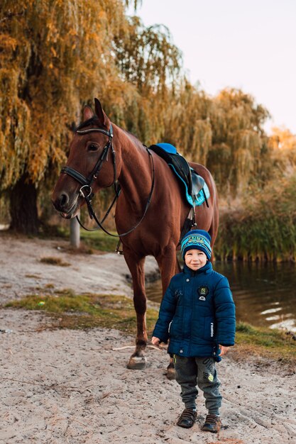 Kleiner Junge, der mit Pferd im Herbstpark geht