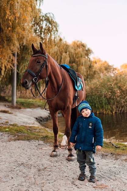 Kleiner Junge, der mit Pferd im Herbstpark geht