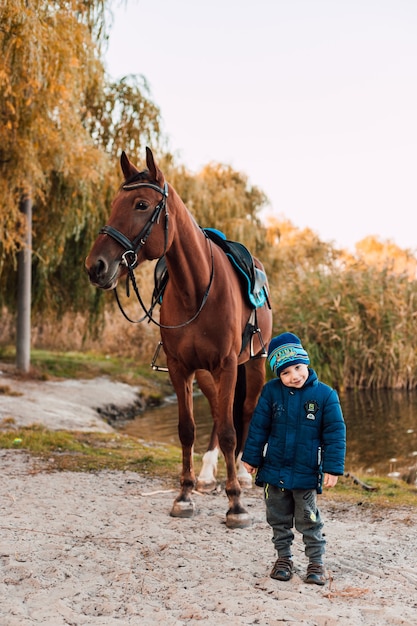 Kleiner Junge, der mit Pferd im Herbstpark geht